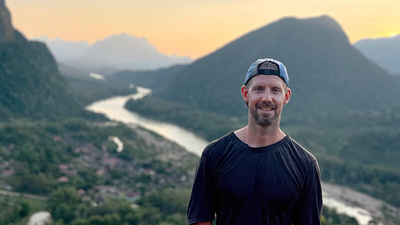 Adam Donovan, vietnamese tour guide, standing in front of majestic rivers and mountains.