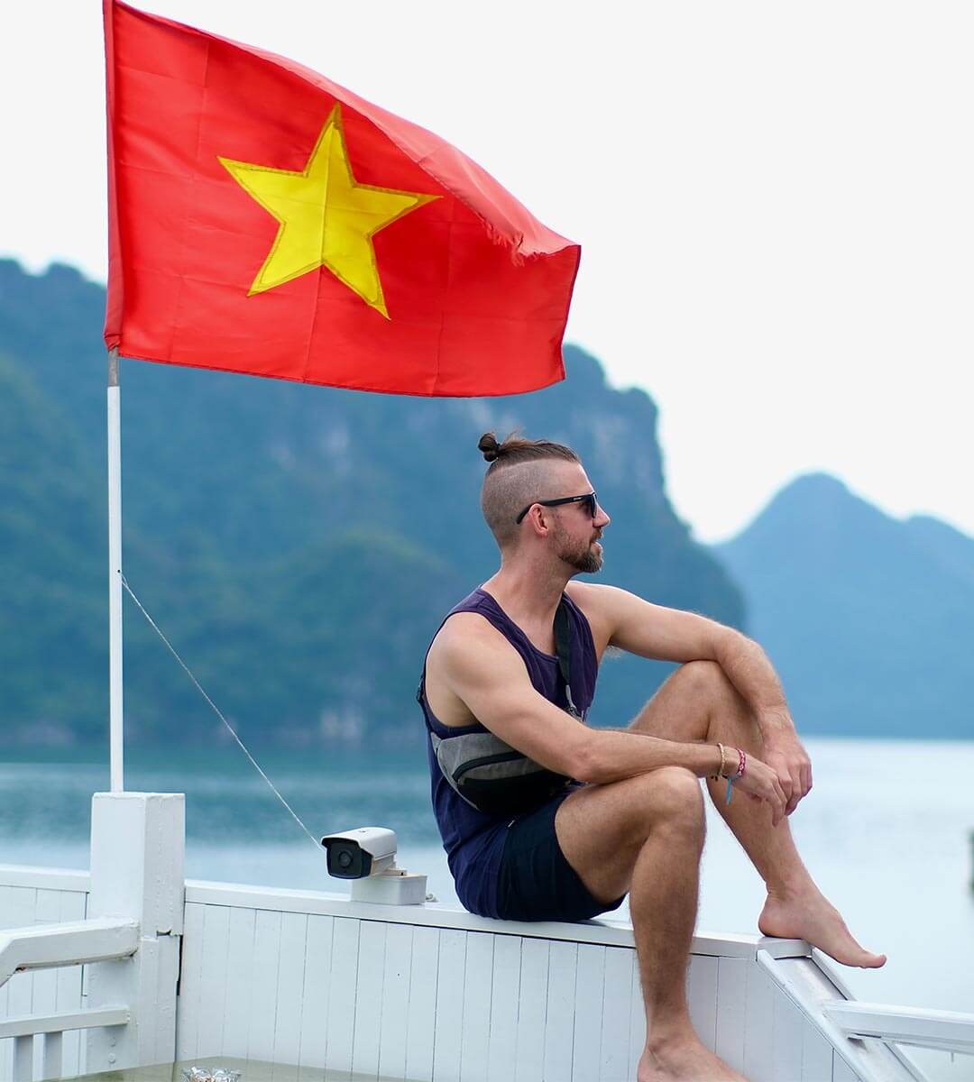 Adam Donovan, owner and tour guide for Authentic adventures, sitting on a boat with the vietnamese flag flapping in the wind.