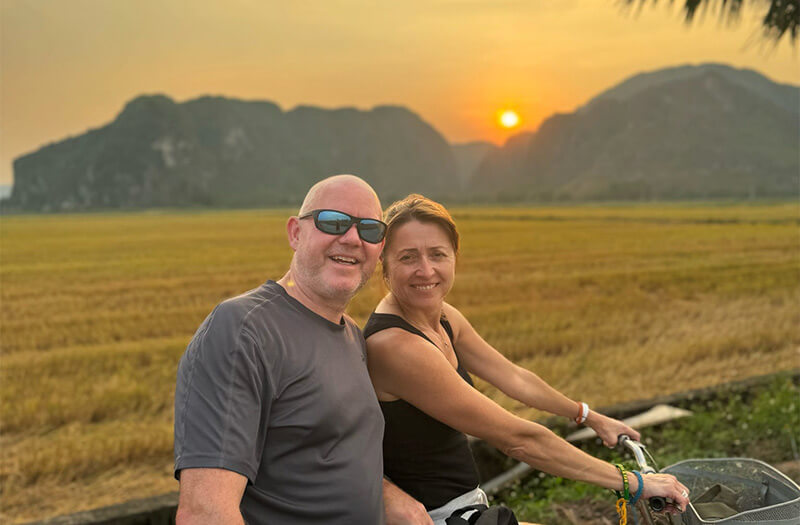 A couple on a bicycle day trip through the rice paddies in Vietnam at sunset.