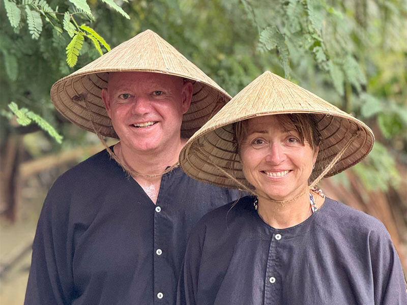 A couple wearing traditional vietnamese rice hats on a tour package holiday with Adam.