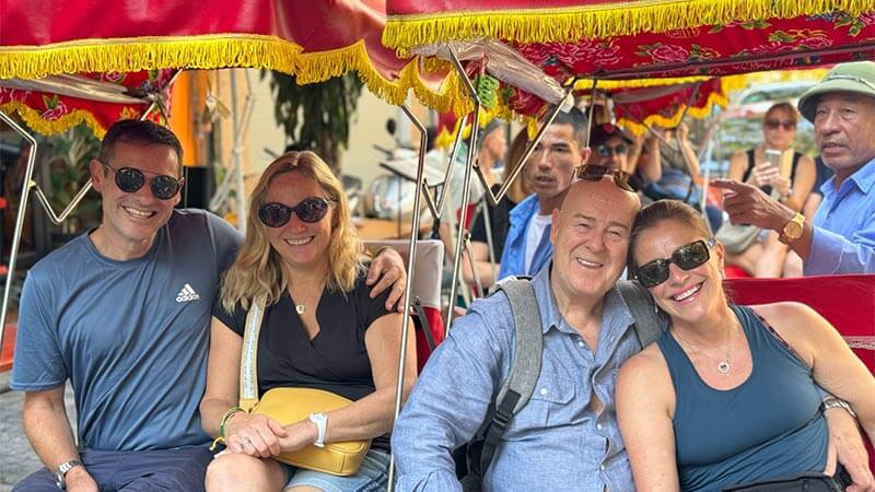 Two couples of a tour with Authentic Adventures sitting in a traditional vietnamese cart with a red roof.